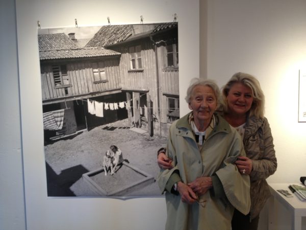 Mor och dotter står tillsammans framför gammal bild på dem
