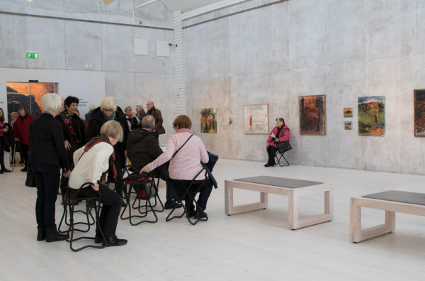En stor vit sal, under ett vernissagetillfälle på Jönköpings läns museum. Människor som sitter och står.