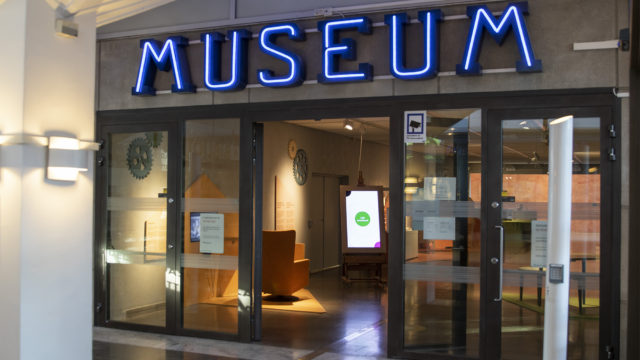 Ingången till museet. Öppna glasdörrar med blåa bokstäver där det står museum ovanför.