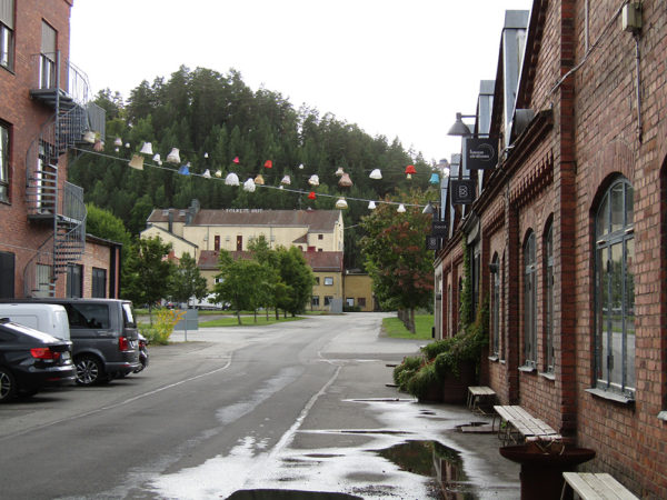 En putsad större byggnad i bakgrunden och i förgrunden bruksmiljö med tegelbyggnader