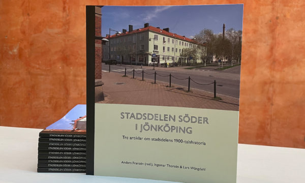 En bok står uppställd lutad mot en hög med böcker. I bakgrunden museets terracottafärgade vägg.