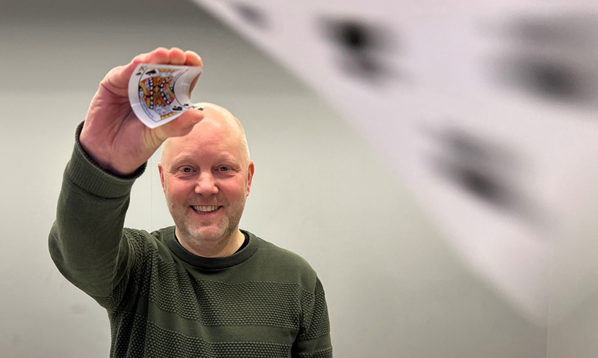 Man med mörk tröja håller upp ett kort i luften samtidigt som det flyger ett kortspelskort bredvid