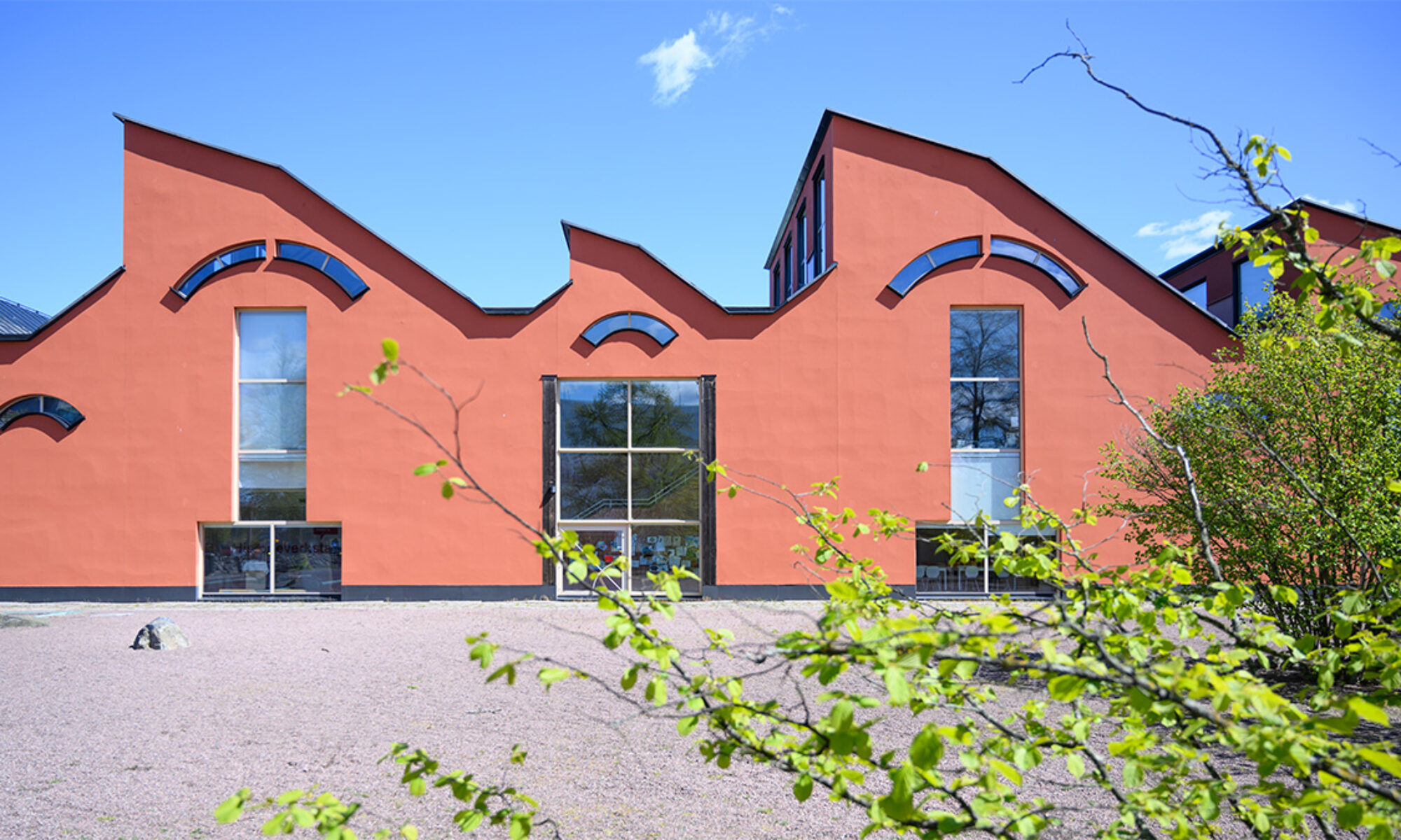 Vågig byggnad med spetsigt tak och blå himmel i bakgrunden.