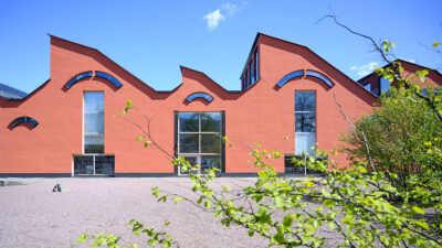 Vågig byggnad med spetsigt tak och blå himmel i bakgrunden.